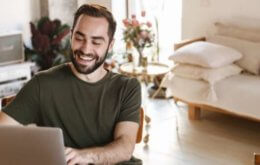 homem sorrindo enquanto trabalha em casa no computador