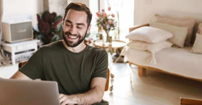 homem sorrindo enquanto trabalha em casa no computador